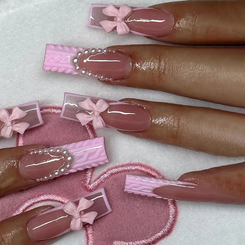 Long coffin press-on nails with pink bows, pearls, and knit texture accents.