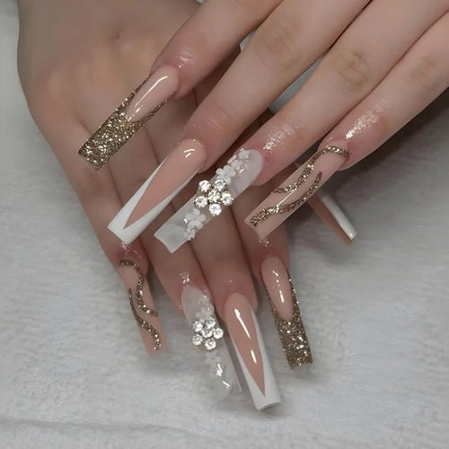 Long coffin press-on nails with glitter, rhinestones, and floral accents. French tip and nude base design.