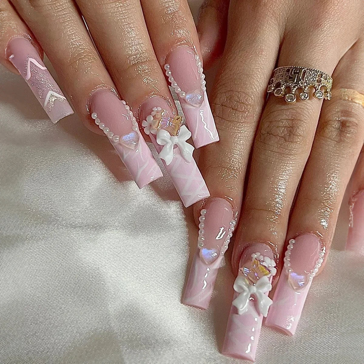 Long coffin-shaped pink false nails with pearl, heart, and bow accents.
