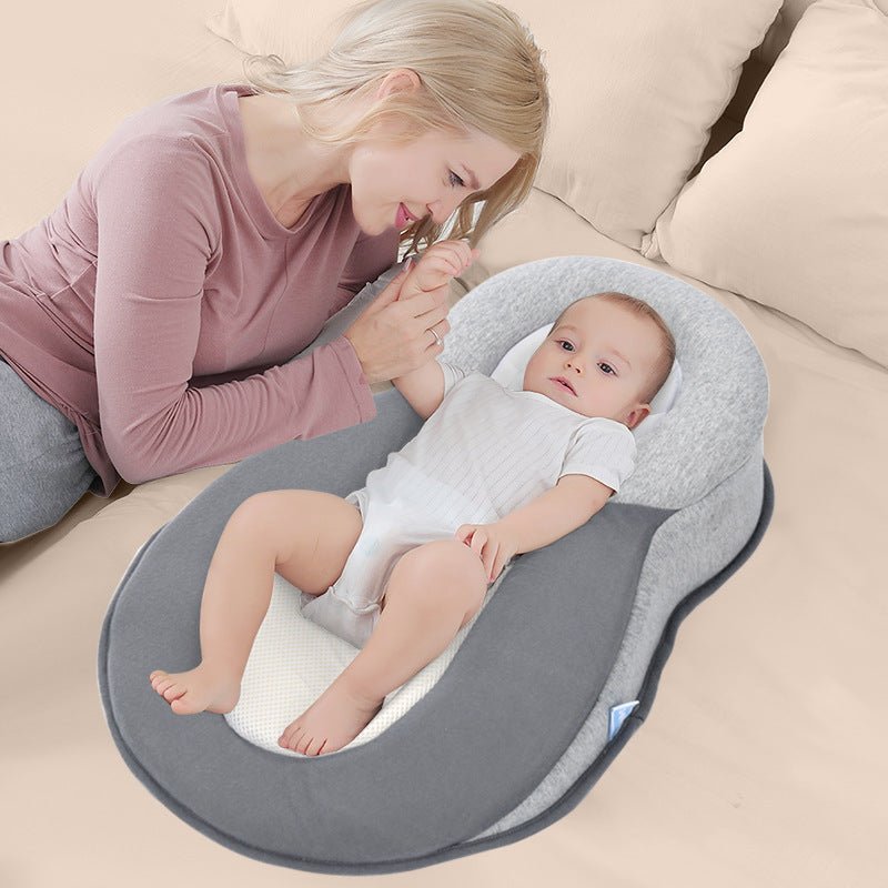 Infant in gray baby nest with head shaping pillow and breathable pad, mother holding baby's hand.