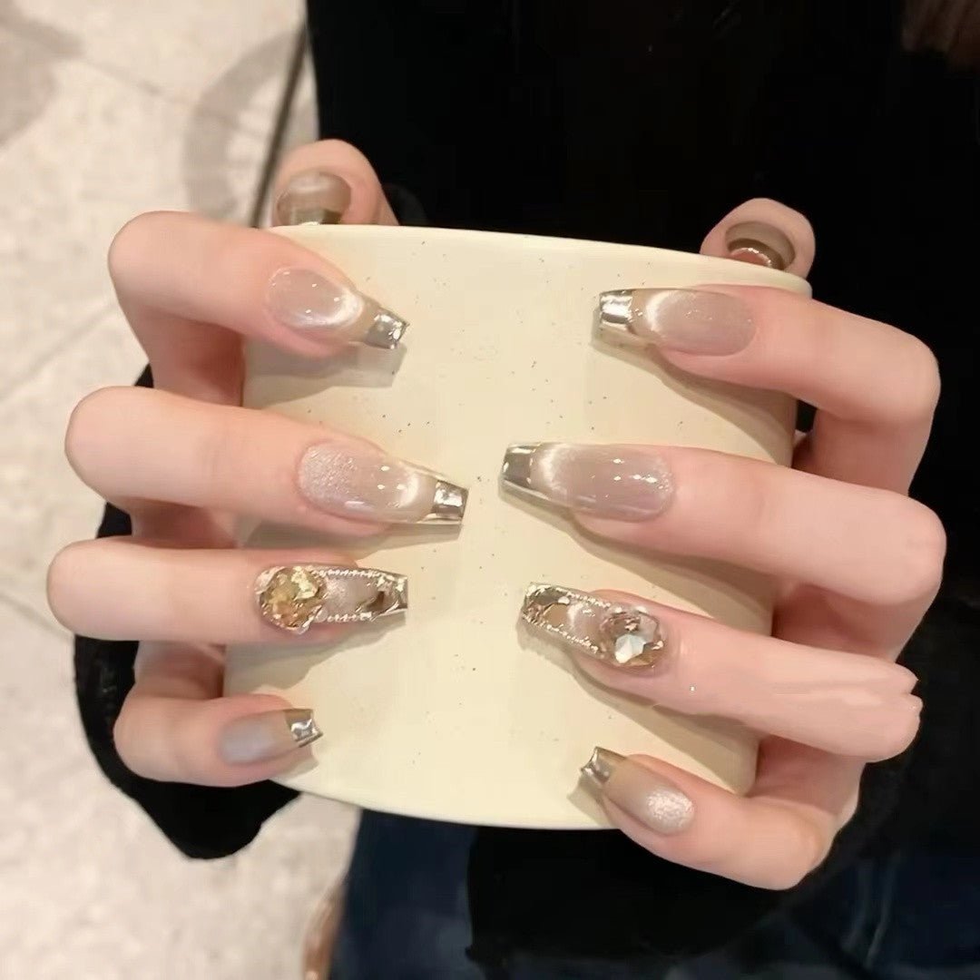 Champagne cat eye press-on nails with silver tips and floral gemstone accents.