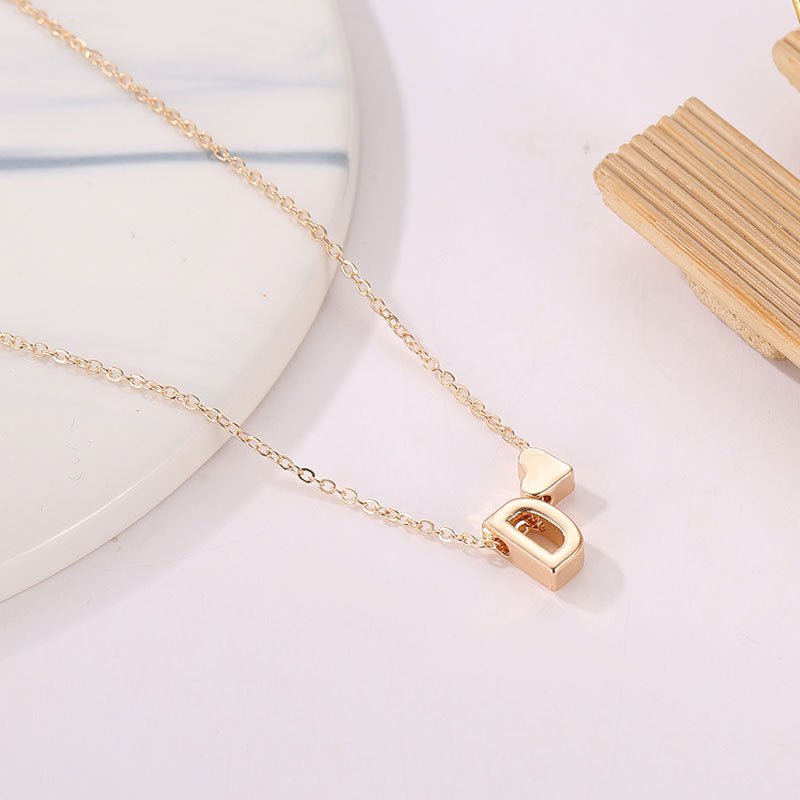Gold initial 'D' necklace with tiny heart charm. Dainty personalized jewelry.